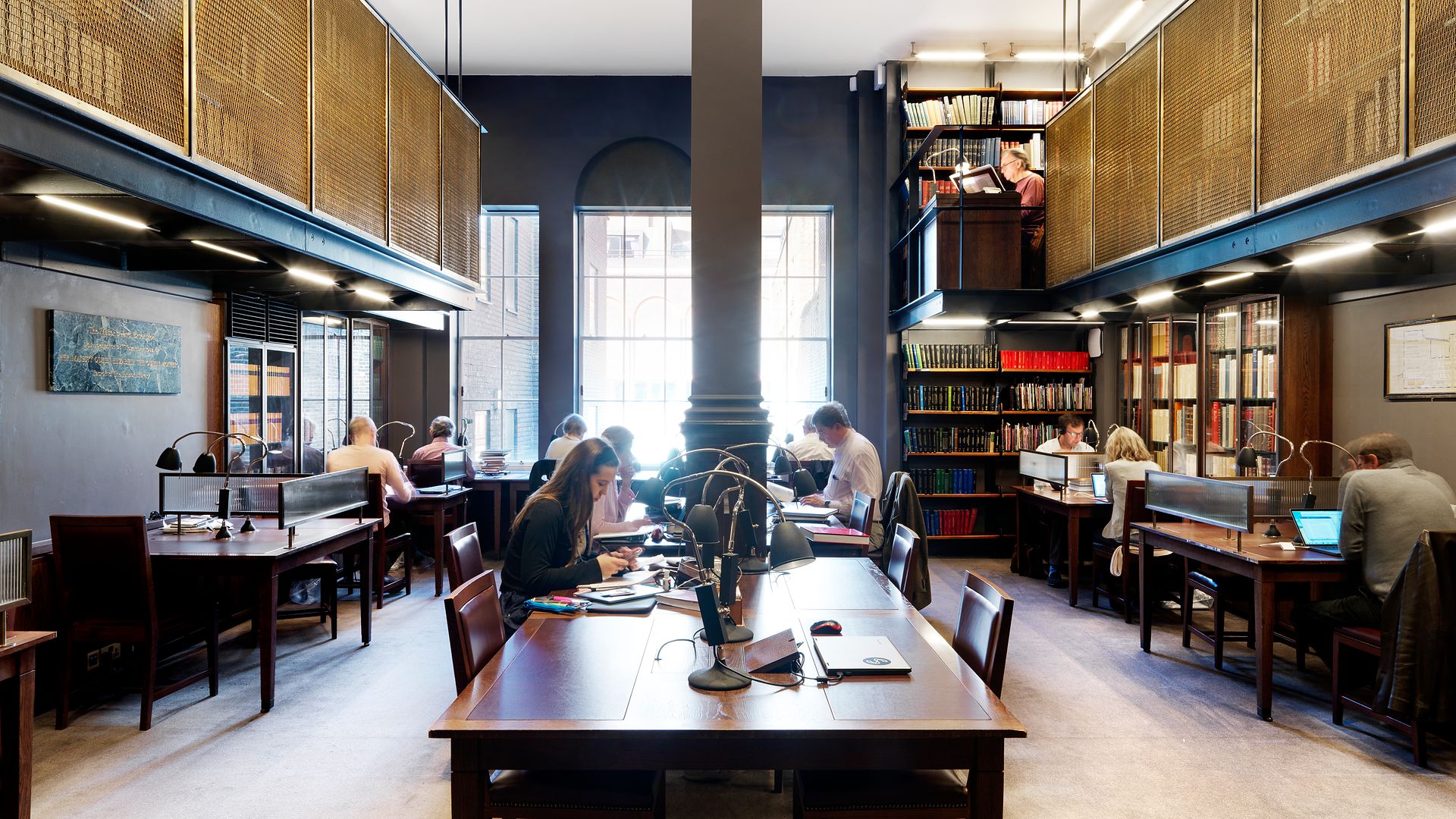 Readers at work under individual lamps along the Writers' Room's dark timber desks.