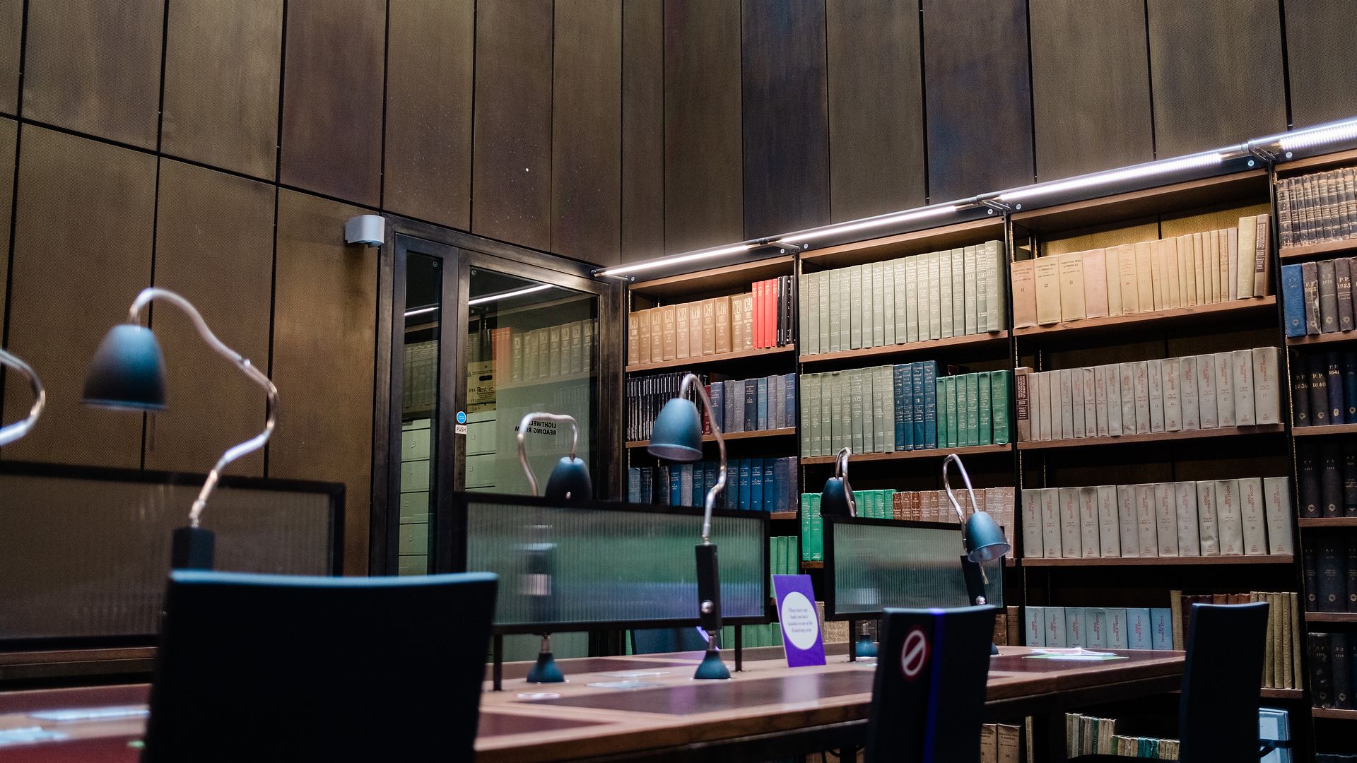 The Lightwell Reading Room's desks and lamps against shelves of green and blue volumes.