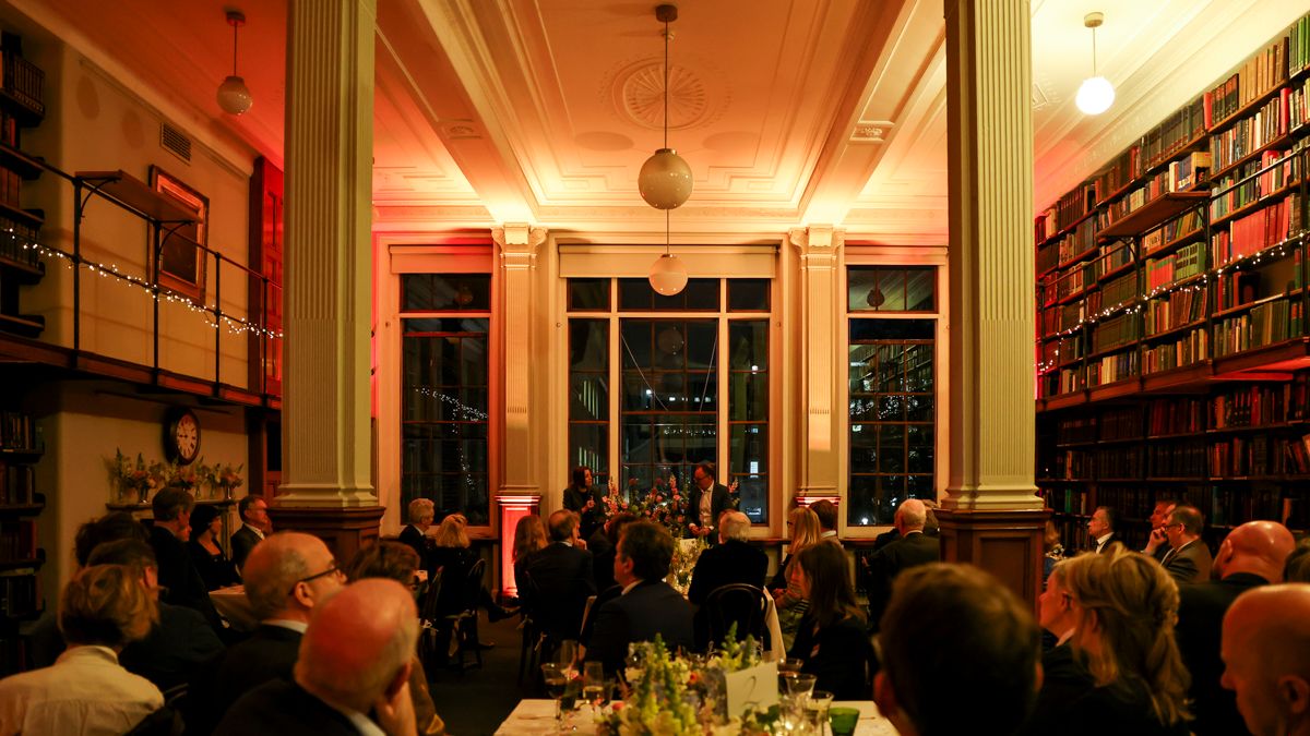Guests seated at a long dinner table beneath the tall windows.