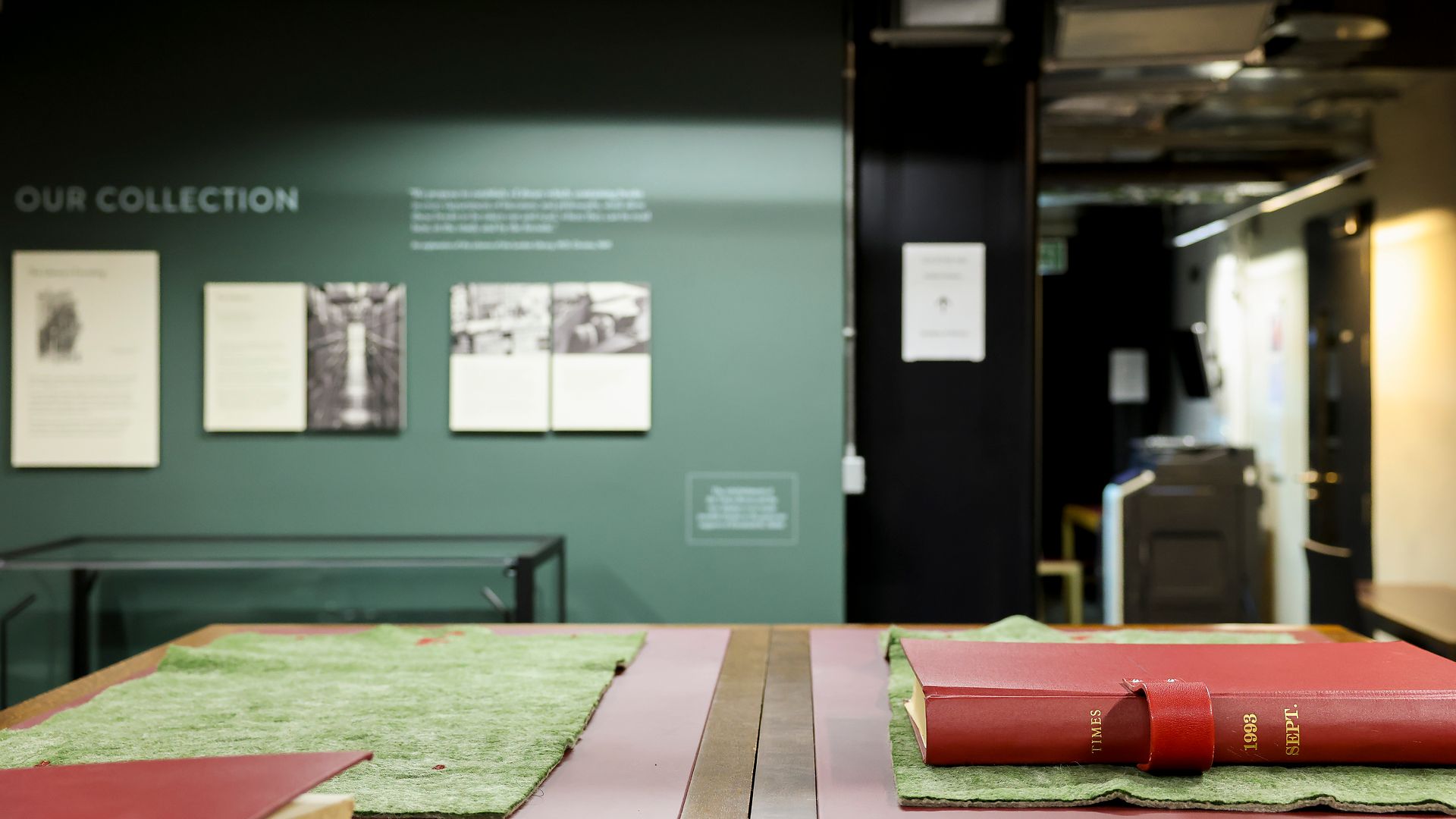 A bound Times volume lettered "1908" on green baize, the Times Room's displays beyond.