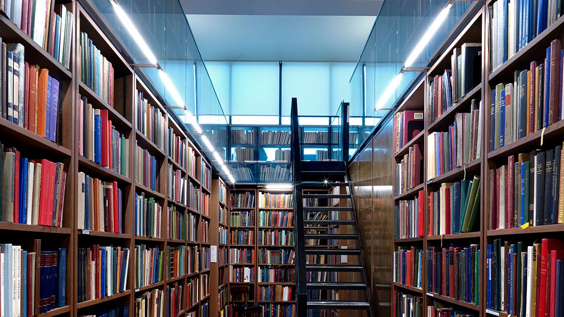 Book-lined aisles of the Art Room, with a steel staircase rising between tall shelves under a glazed ceiling.
