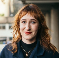 Portrait of Jasmin, a white woman with red hair in a dark top. 