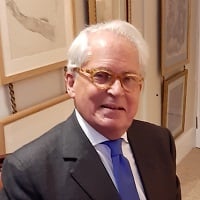 Portrait of Alain, a white man with glasses and white hair wearing a suit and blue tie. 