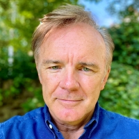 A portrait of Neil, a white man in a blue shirt, taken in a garden.