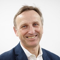 Portrait of John in a blue suit white shirt against a white background.