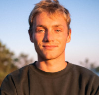 Portrait of Elliot, a white man with blonde hair in a grey top, at golden hour.