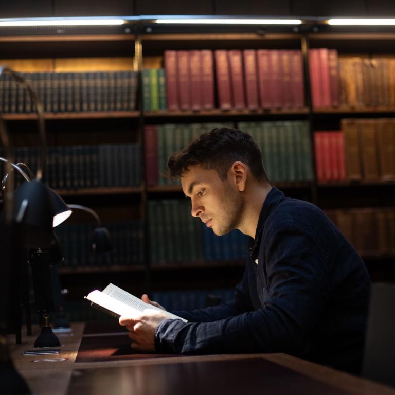 A member reading at a desk beneath shelves of red and green bound volumes.
