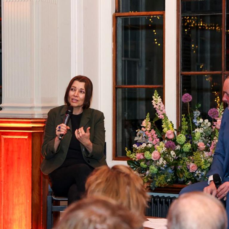 Two speakers in conversation with microphones beside a vase of flowers at the dinner.