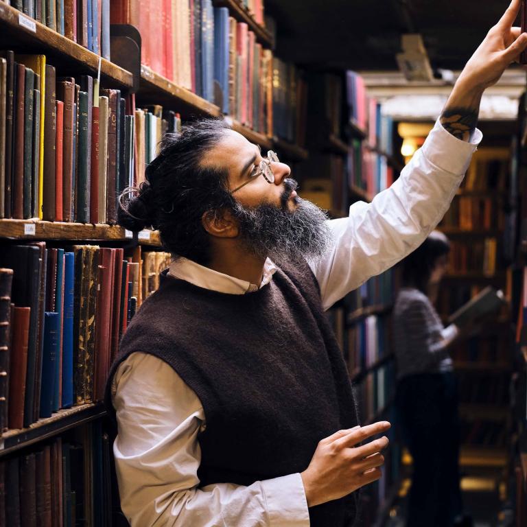 A member of staff reaches up to a high shelf in the bookstacks.