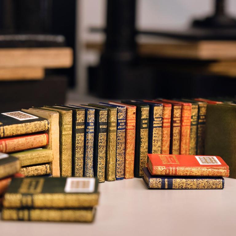 Rows of gilt-decorated miniature books arranged on a bindery workbench.