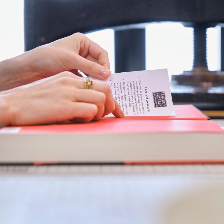 Hands tucking a care-and-use leaflet into a pink-bound book beside a press.