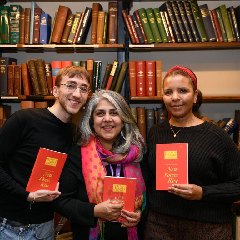 Three writers laugh together as someone photographs them holding the anthology.