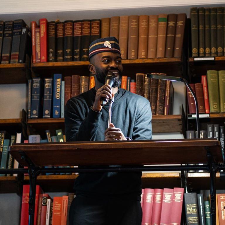 Inua Ellams performs at a lectern in front of the Library's bookshelves.