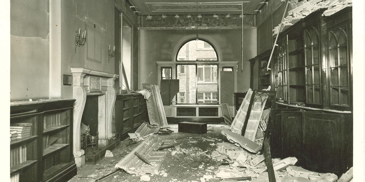 Bomb damage in a Library room, plaster and broken shelving covering the floor.