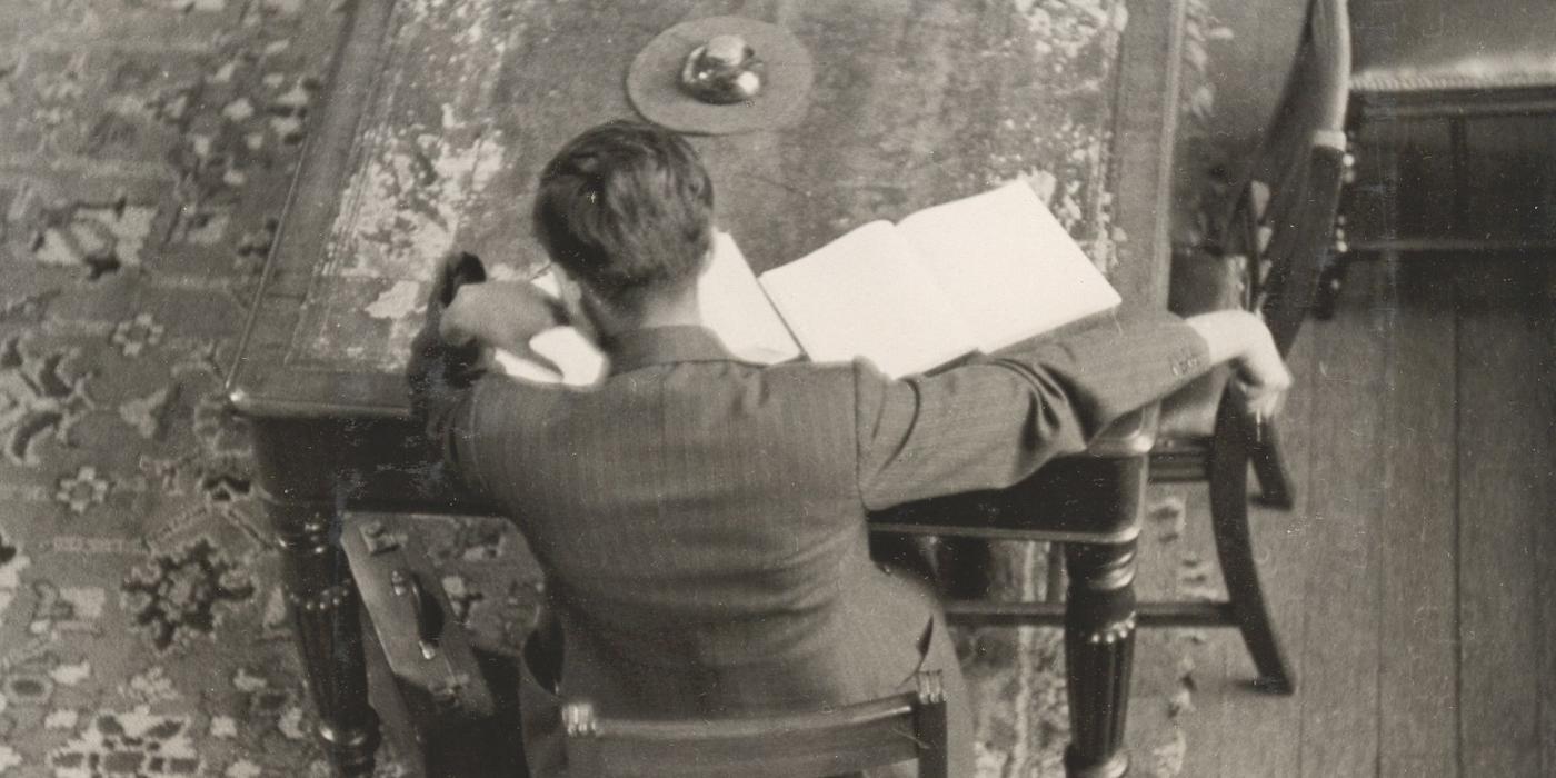 A reader seen from behind, working at a table with an open book and papers, 1935.