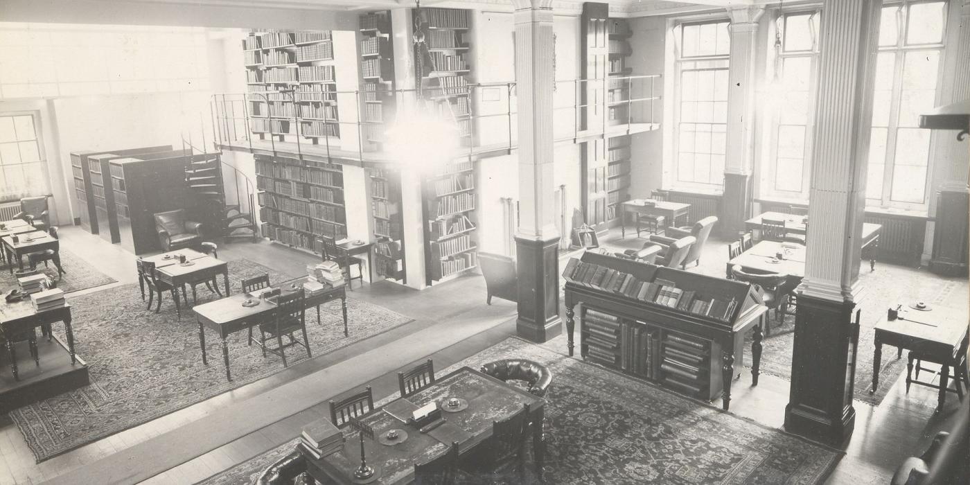 A galleried reading room with tables, armchairs and book presses, photographed in 1935.