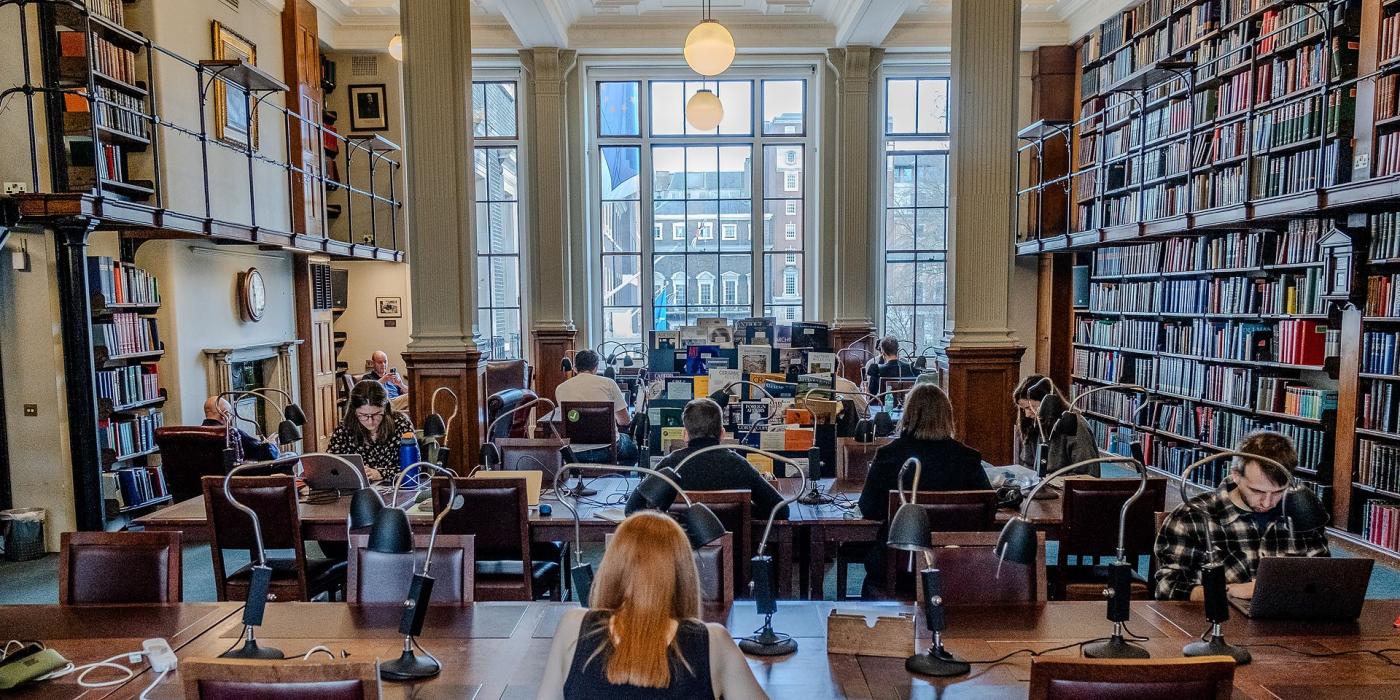 The Reading Room busy with members at desks beneath tall windows and hanging globe lights.