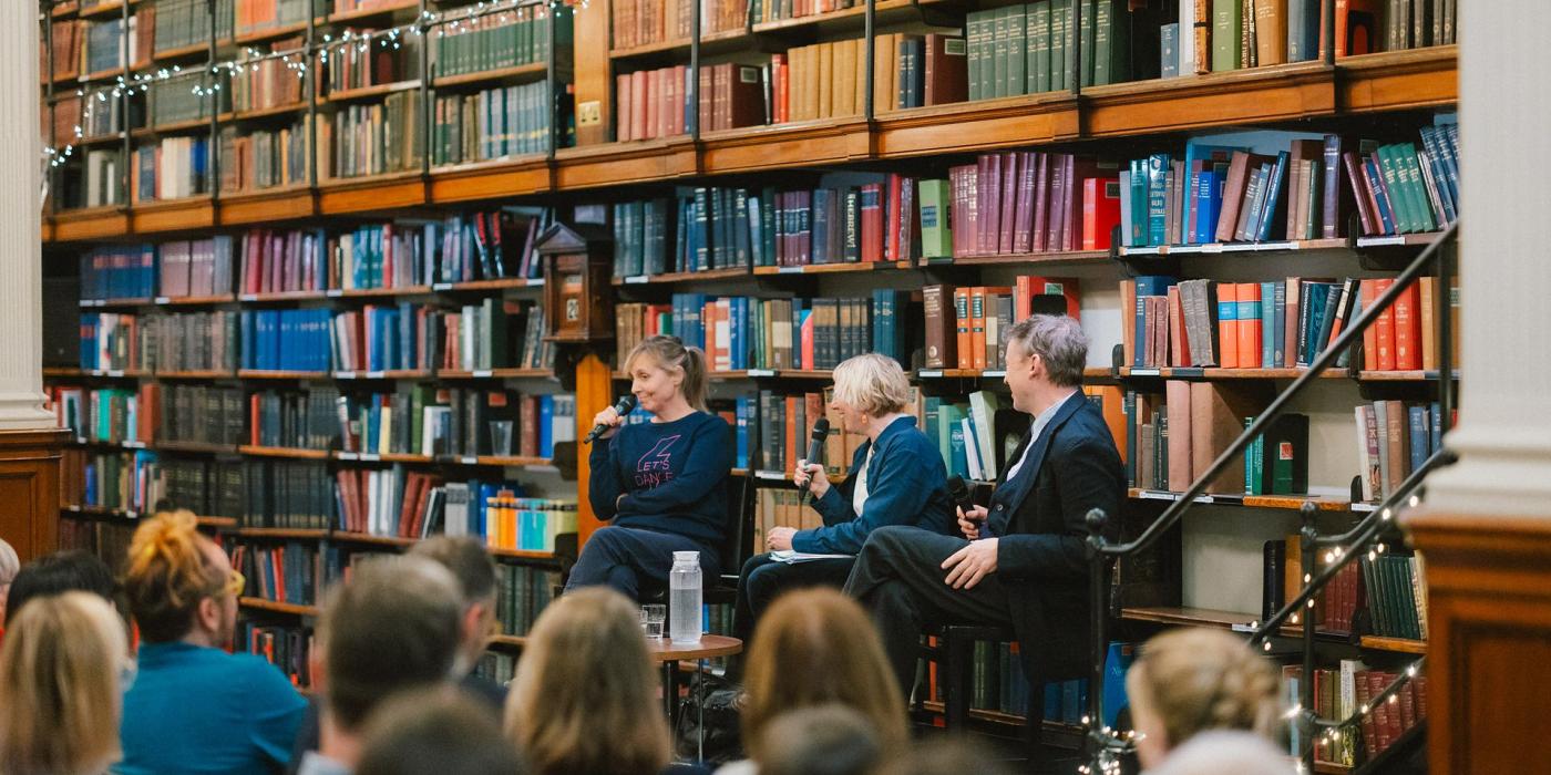Three panellists in conversation, fairy lights strung along the shelves behind them.