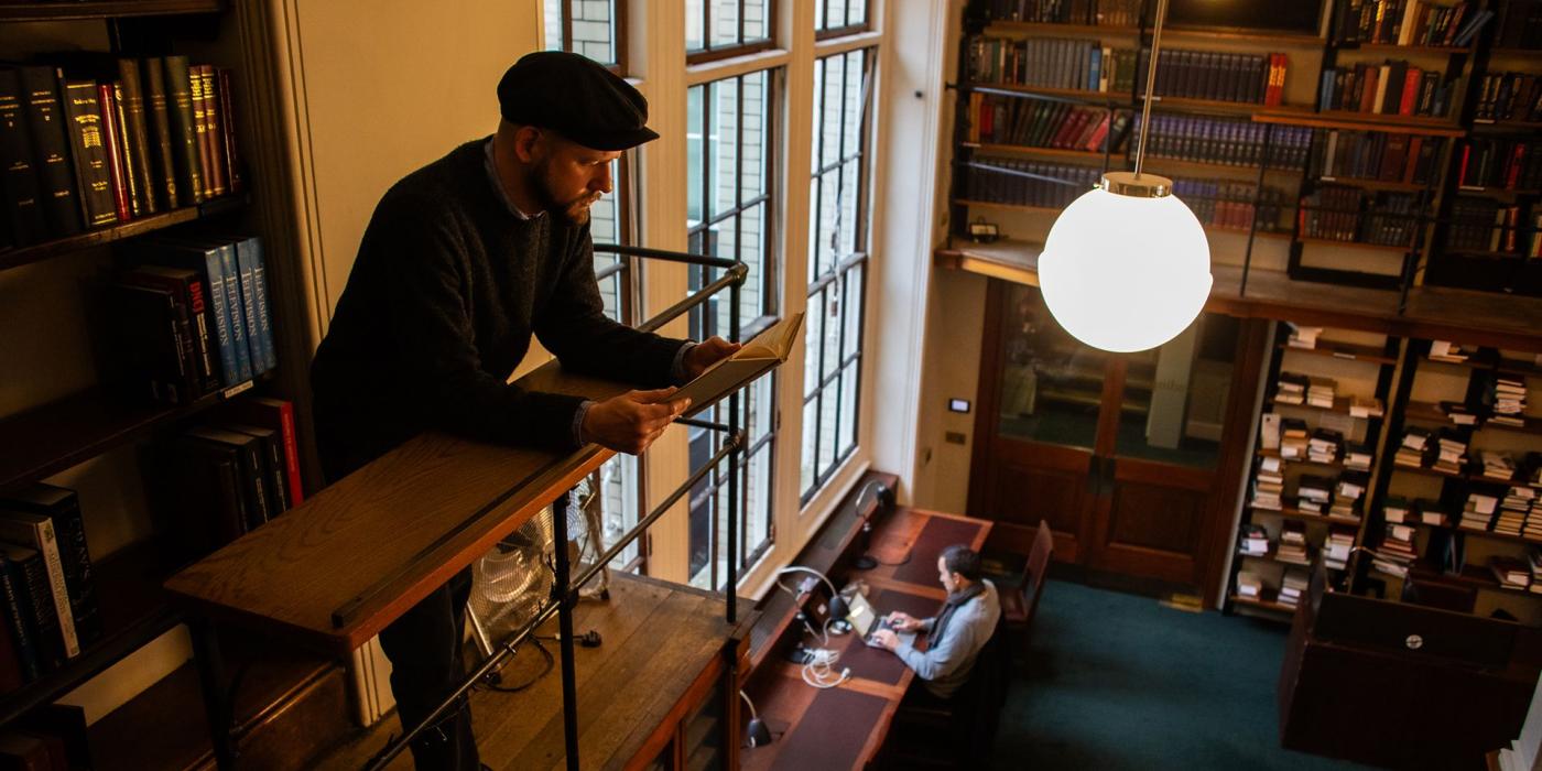 A member reading at a gallery lectern above the reading room, readers at desks below.