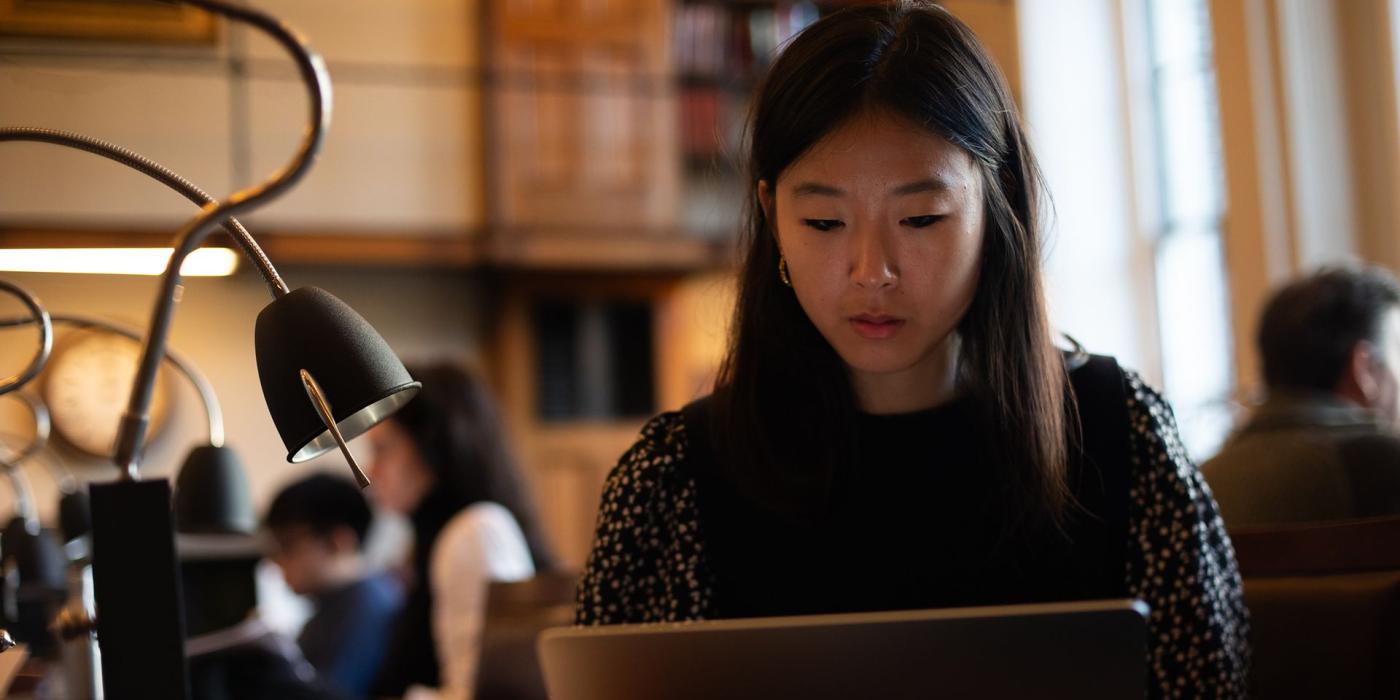 A member working on a laptop at a lamp-lit reading desk.