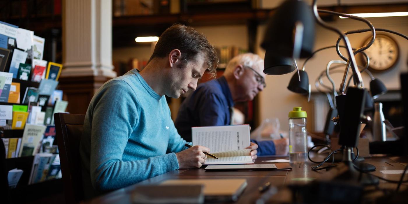 A member making notes from an open book at a reading desk.