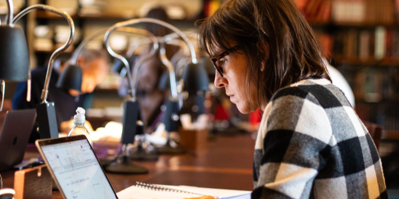 A member typing on a laptop with a notebook open beside her.