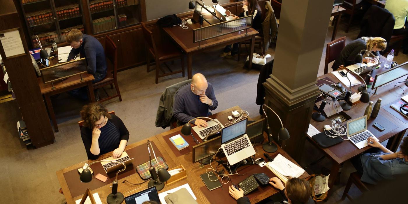 Members at work along a shared desk of laptops and reading lamps, seen from above.