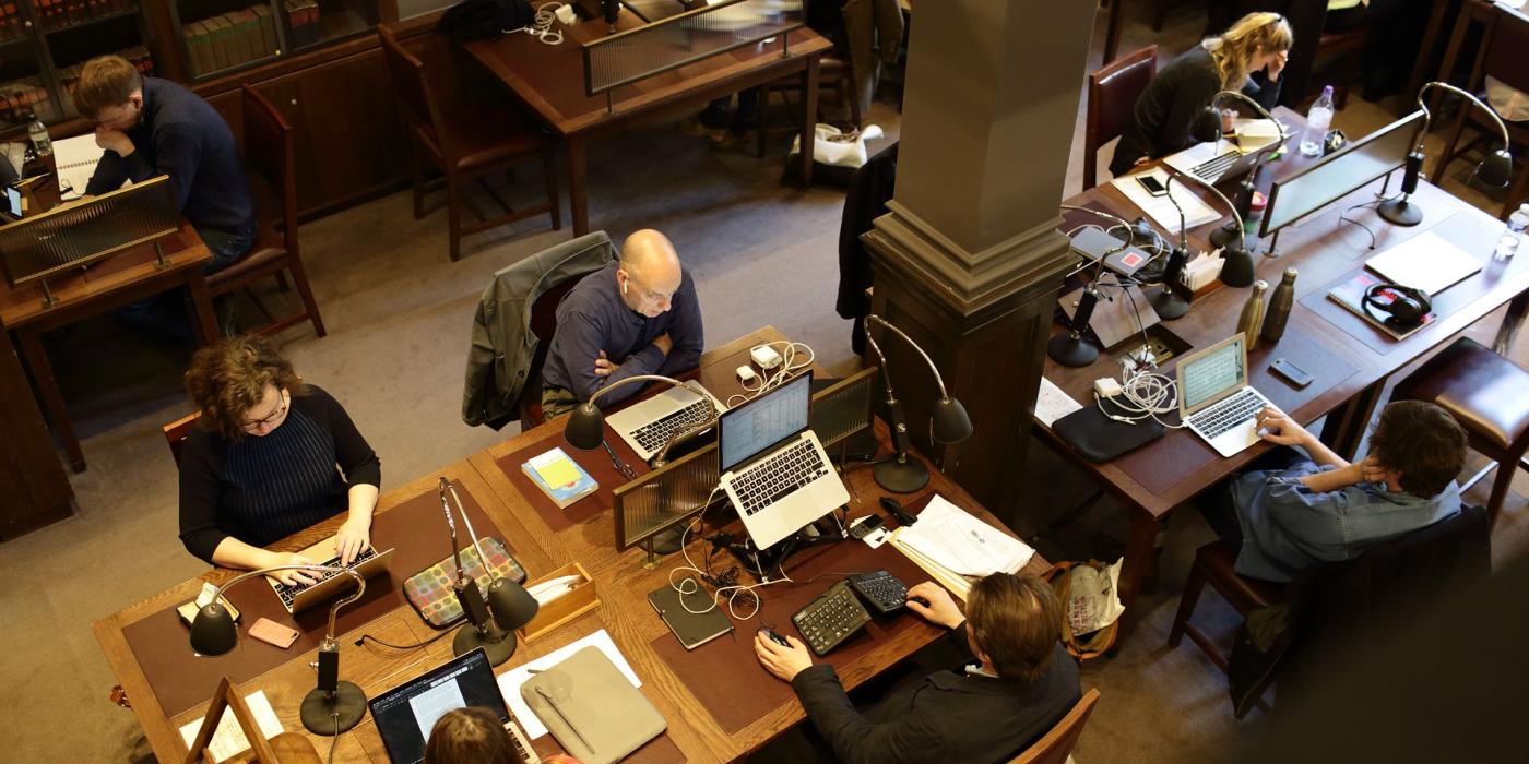 A row of members working at laptops under individual lamps, viewed from the gallery.