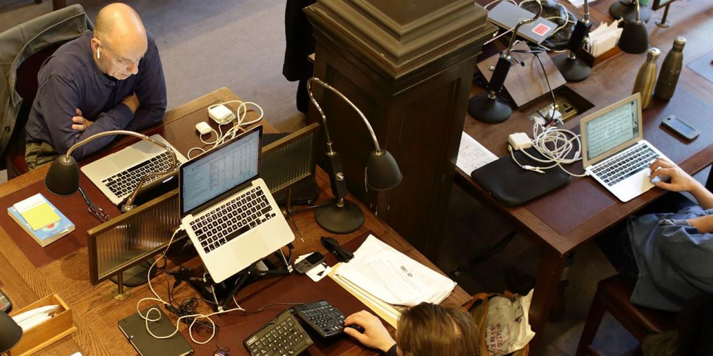 A row of members working at laptops under individual lamps, viewed from the gallery.