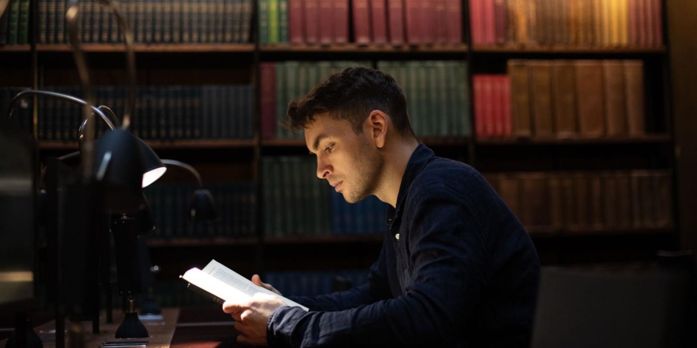 Man reading, book shelves behind him