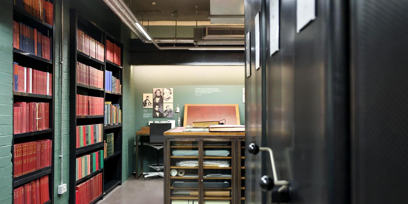 A view between bookstacks into the Times Room, with a plan chest and reading lectern.