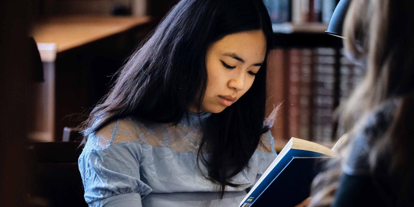 Two readers work together, one holding an open blue-bound book.