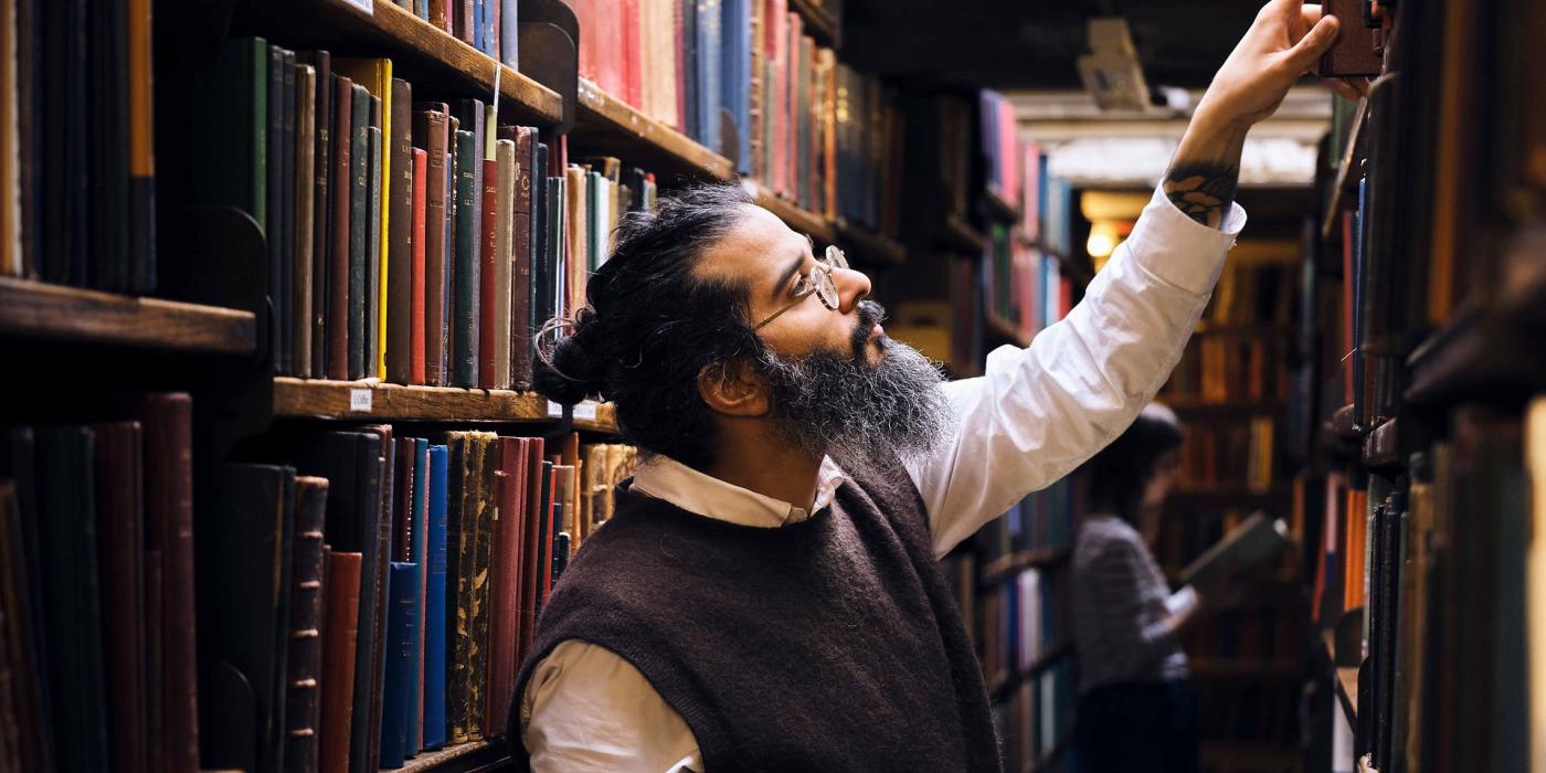 A member of staff reaches up to a high shelf in the bookstacks.