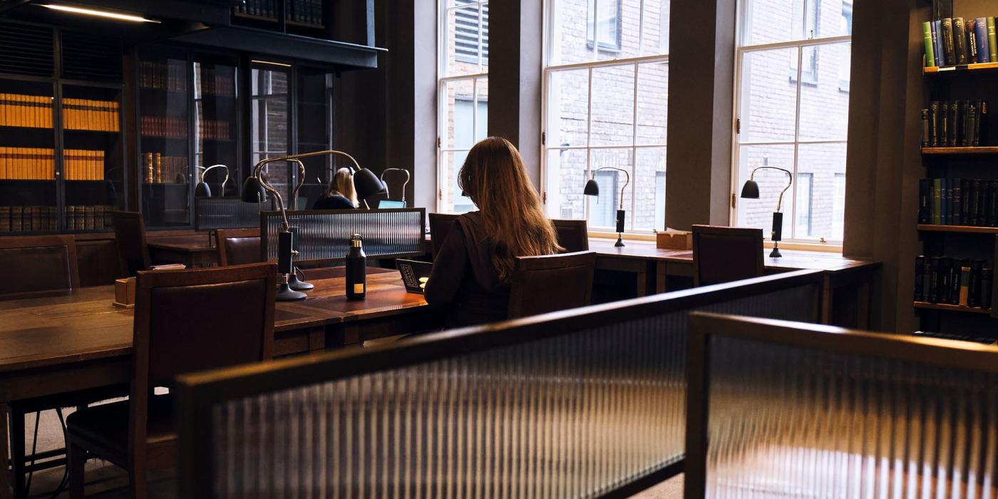 A member working at a desk beside tall windows, seen through a ribbed glass desk screen.