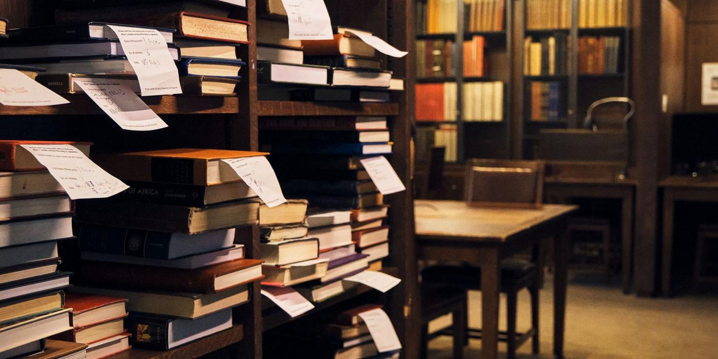 Shelves of books interleaved with handwritten reservation slips, a reading room table beyond.