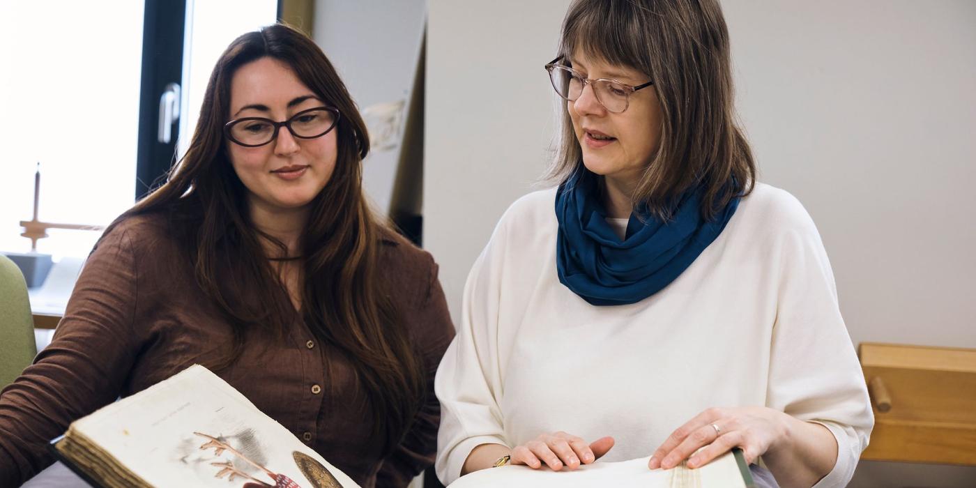 Two members of staff looking through a large folio of hand-coloured natural history plates.