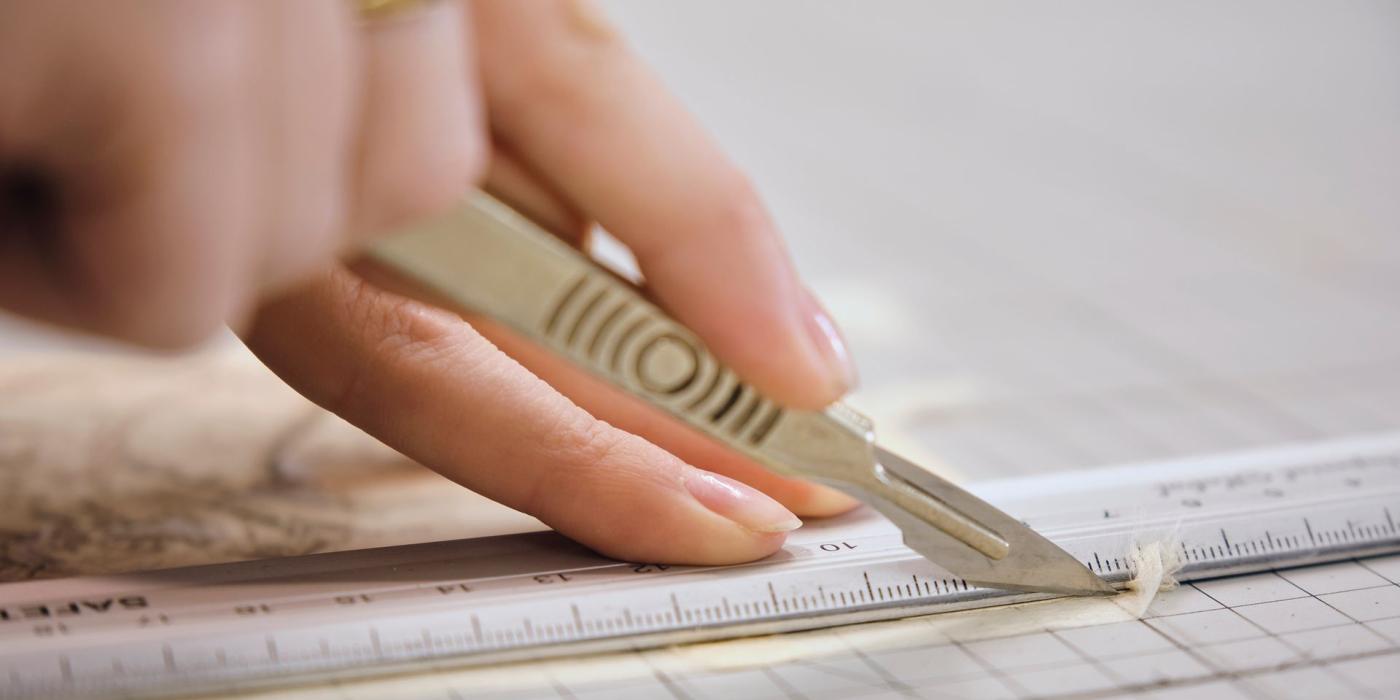A conservator trimming linen with a scalpel against a steel rule on a cutting mat.