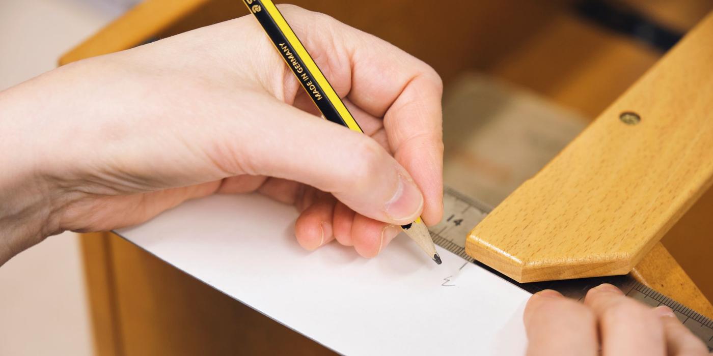 A conservator marking a measurement on card with a pencil and wooden rule.