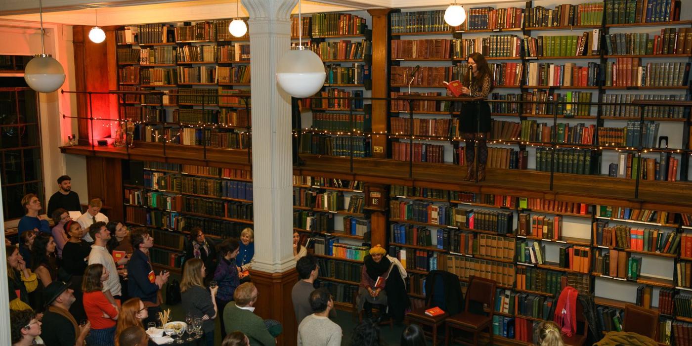The audience listening in the book-lined hall as a writer reads from the gallery.