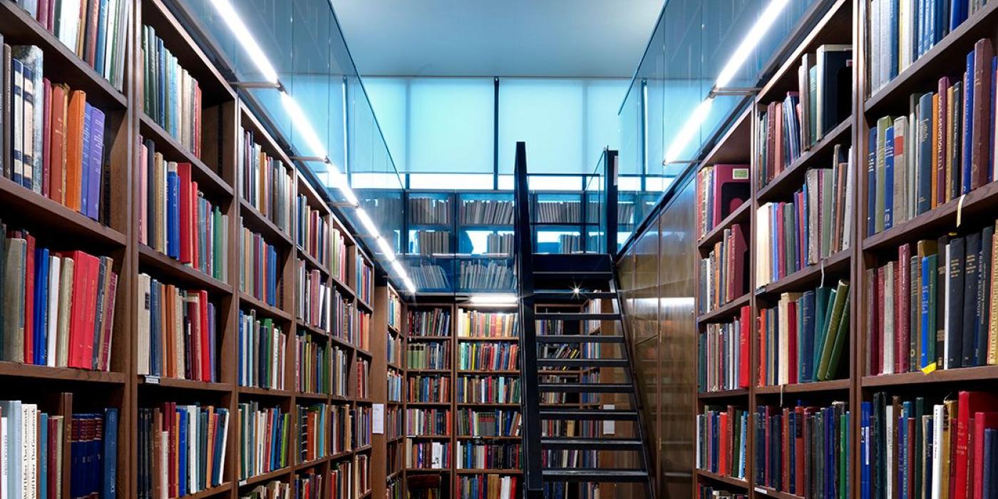 Book-lined aisles of the Art Room, with a steel staircase rising between tall shelves under a glazed ceiling.