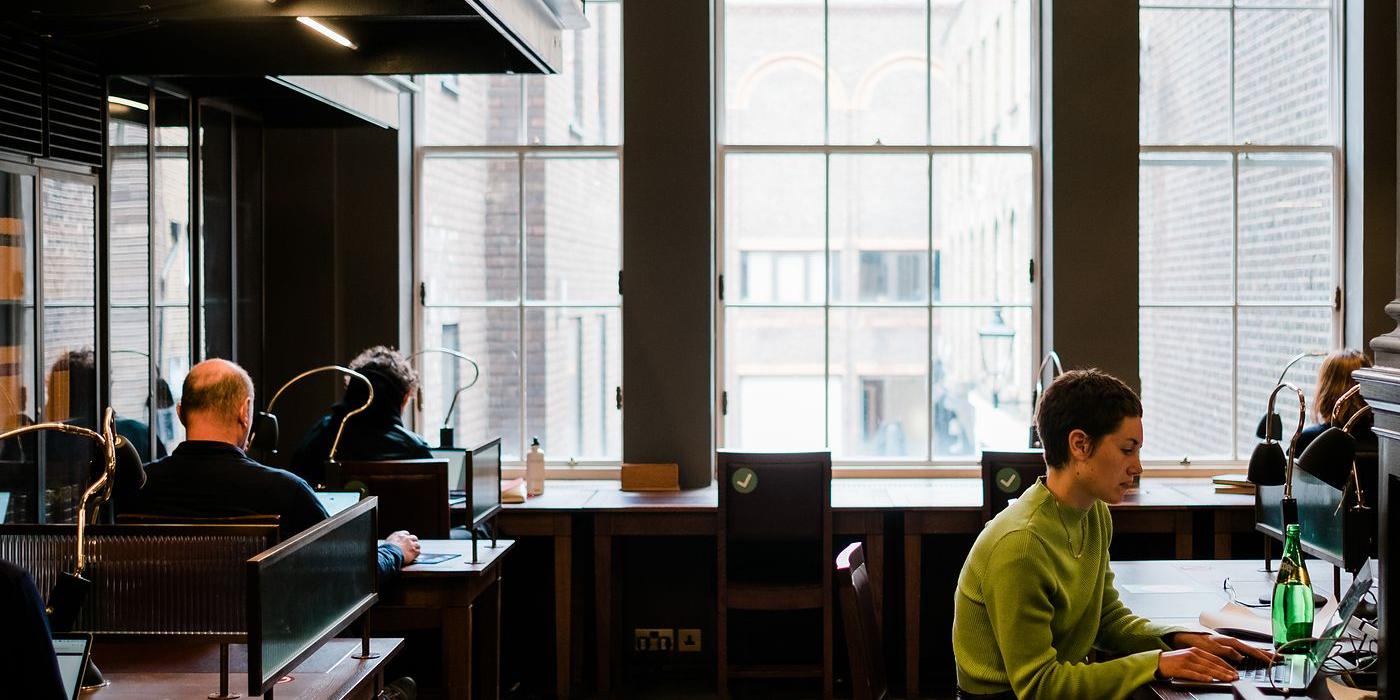 A member working at a desk in the Writers' Room beside a tall arched window.