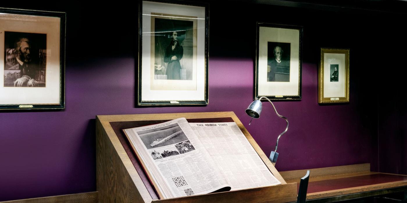 Old newspaper displayed and images of men from 18th-19th century on the wall
