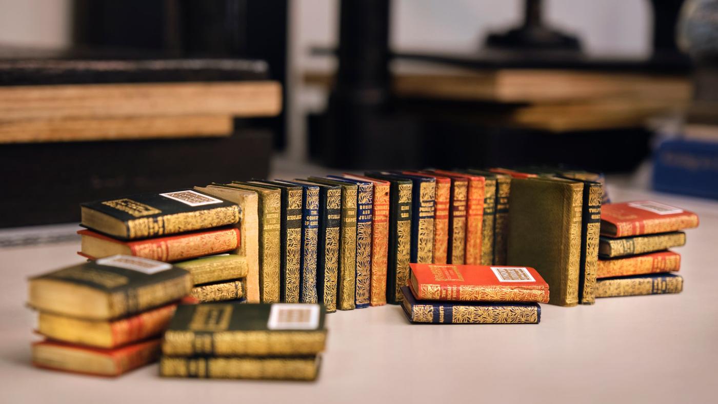 Rows of gilt-decorated miniature books arranged on a bindery workbench.